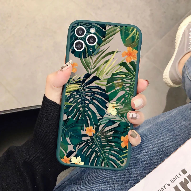 A close-up photo of a hand holding a clear phone case with a tropical leaf and flower design. 